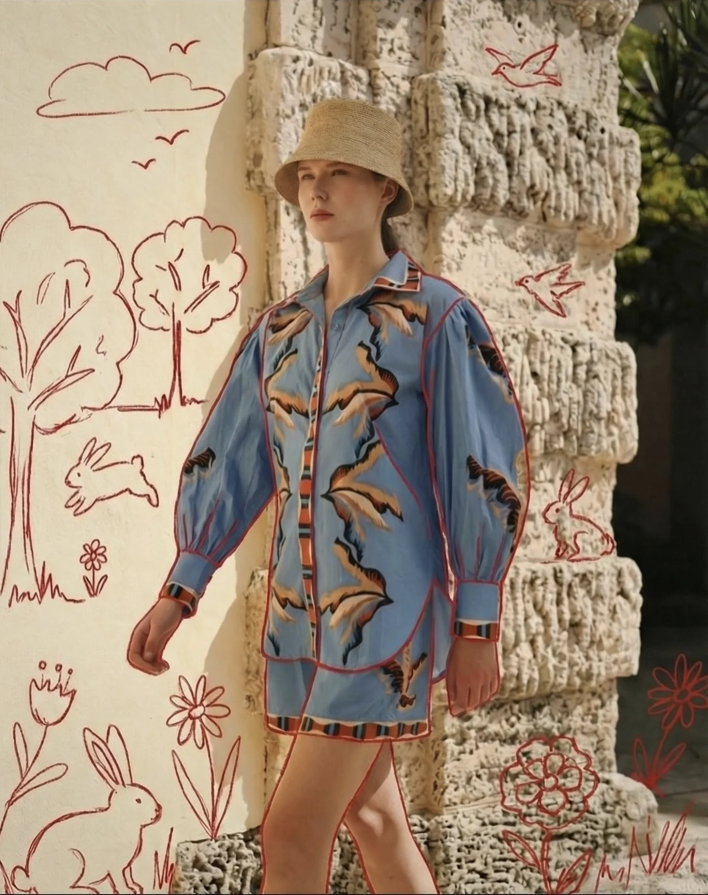 Modelo con camisa estampada caminando frente a un muro con dibujos de conejos y flores